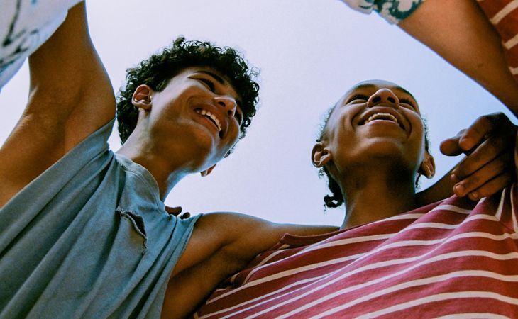 Mulher sorridente sentada numa cama, a abraçar uma criança que segura um pequeno ramo de tulipas brancas, num quarto luminoso e acolhedor com luz natural. 